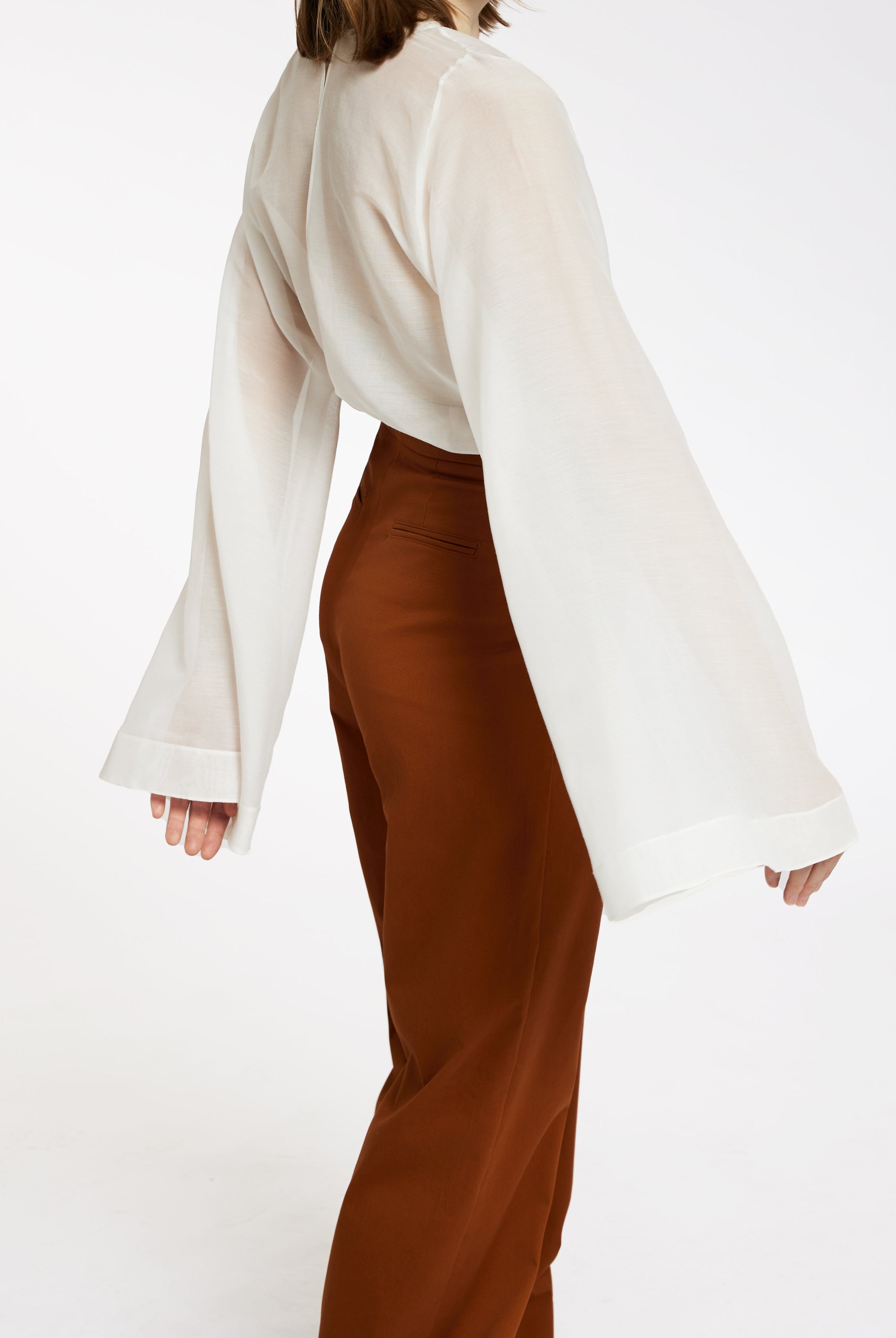 Femeie in bluza alba cu maneca larga si pantaloni lungi teracota