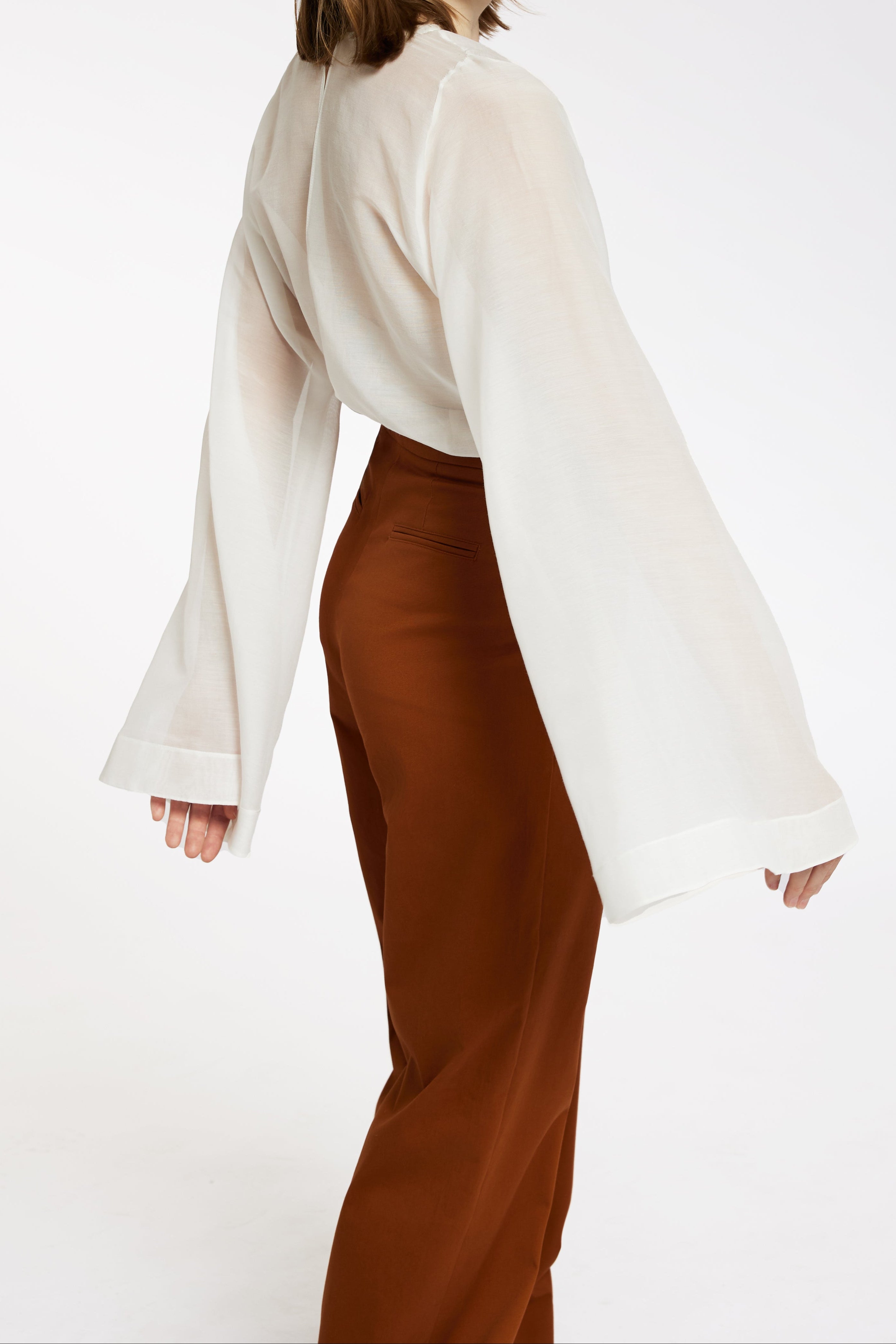 Femeie in bluza alba cu maneca larga si pantaloni lungi teracota