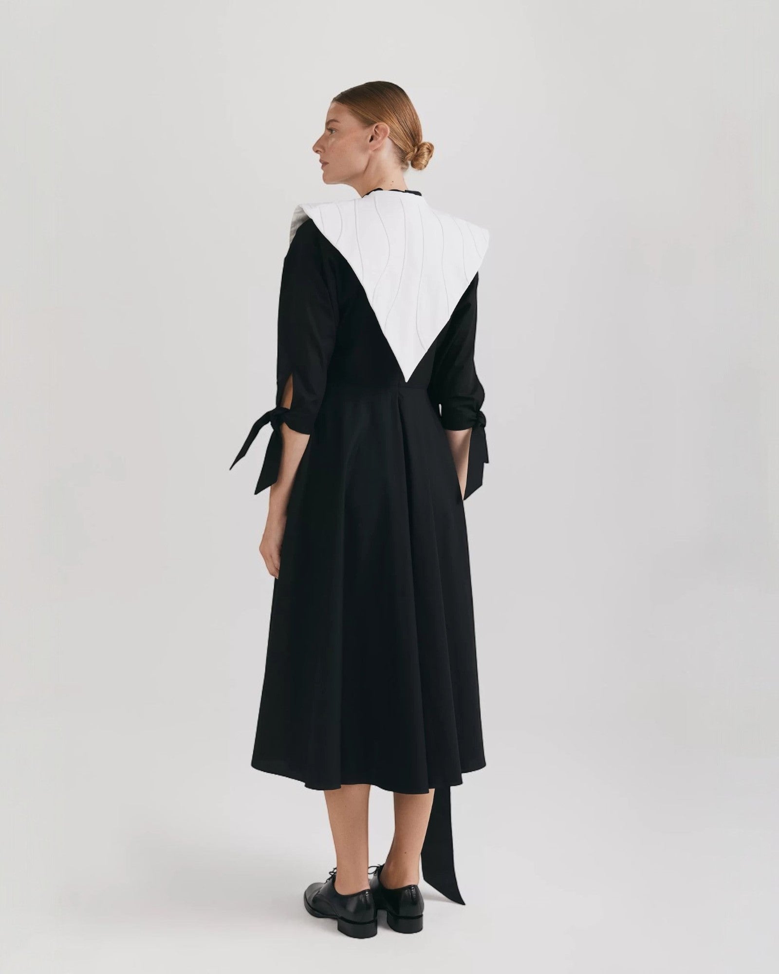 Ipanomi black organic cotton midi dress with flared skirt, 3/4 raglan sleeves, mandarin collar, and tie details.