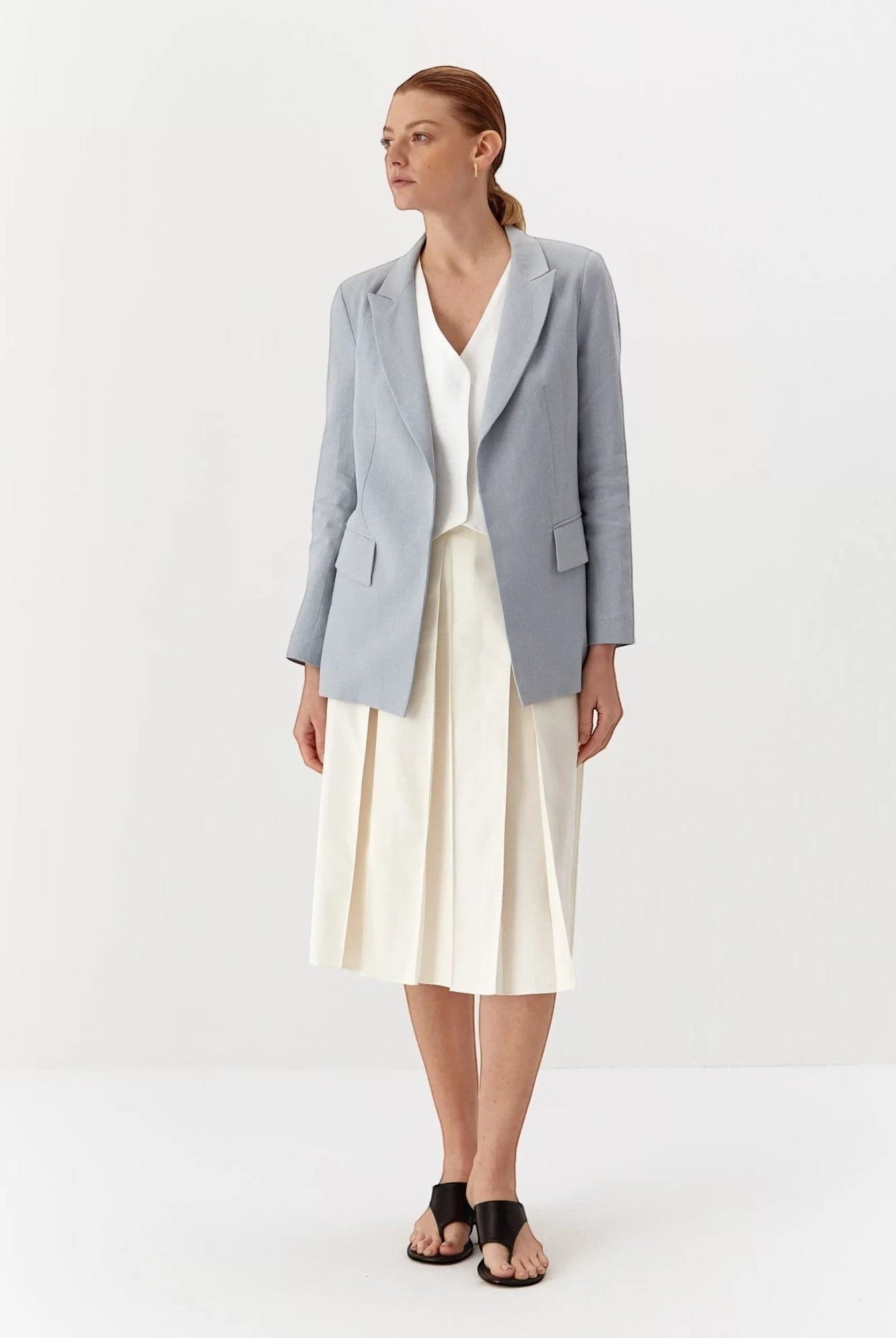 Ipanomi light blue linen blazer with lapel collar, flap pockets, and a tailored fit. Worn by a model with a white top and cream skirt.
