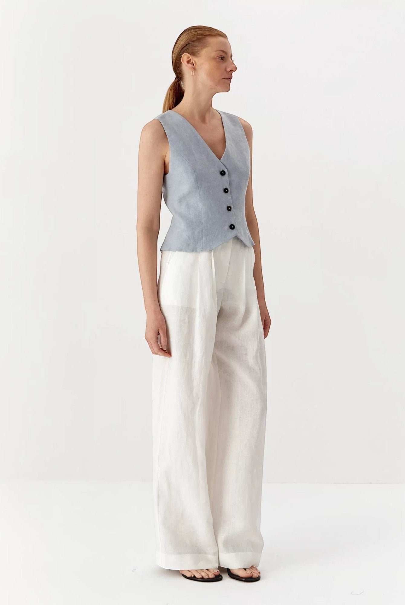 Ipanomi light blue pure linen short vest with V-neck and black buttons, worn by a model.