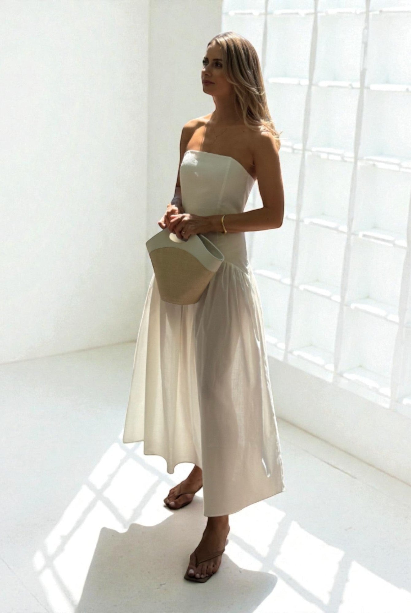 Ipanomi strapless white cotton poplin corset and maxi skirt set with a straw and leather handbag.
