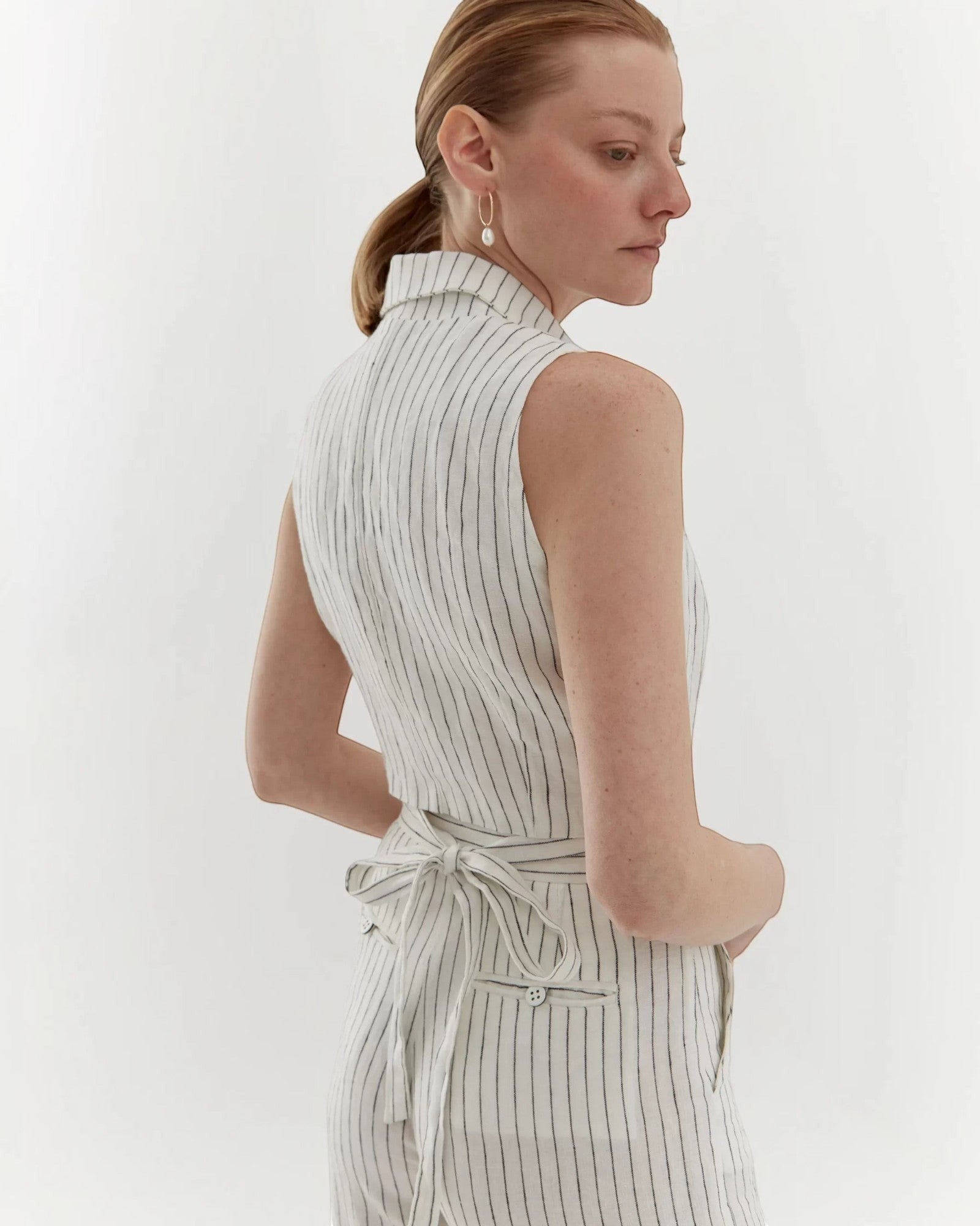 Ipanomi white linen trousers with black pinstripes, high waist, straight leg, and tie waist. Model wears size S.