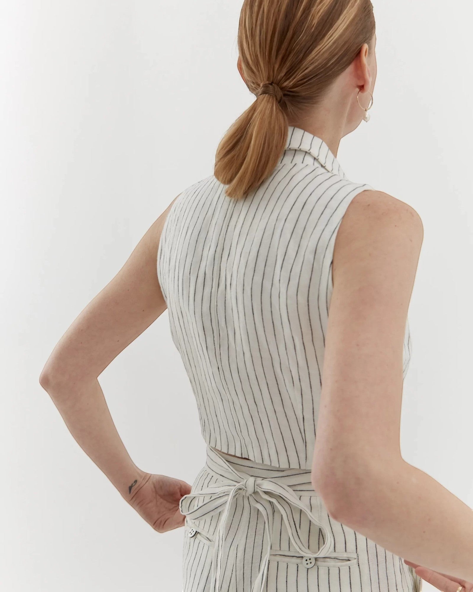 Ipanomi white linen trousers with black pinstripes, high waist, straight leg, and tie belt. Model is wearing size S.