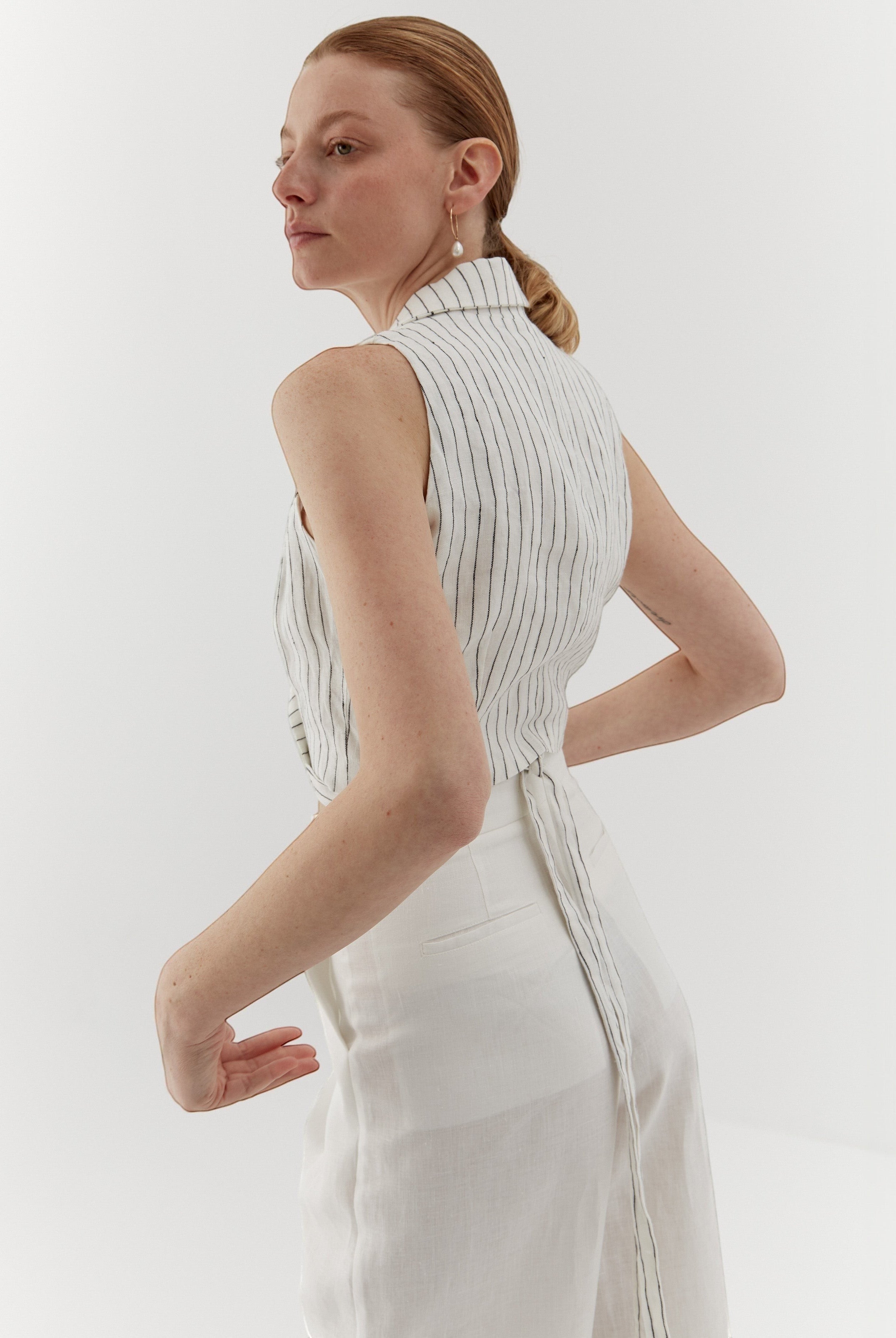 Ipanomi white linen vest with fine black pinstripes, featuring a wrap closure and adjustable tie.