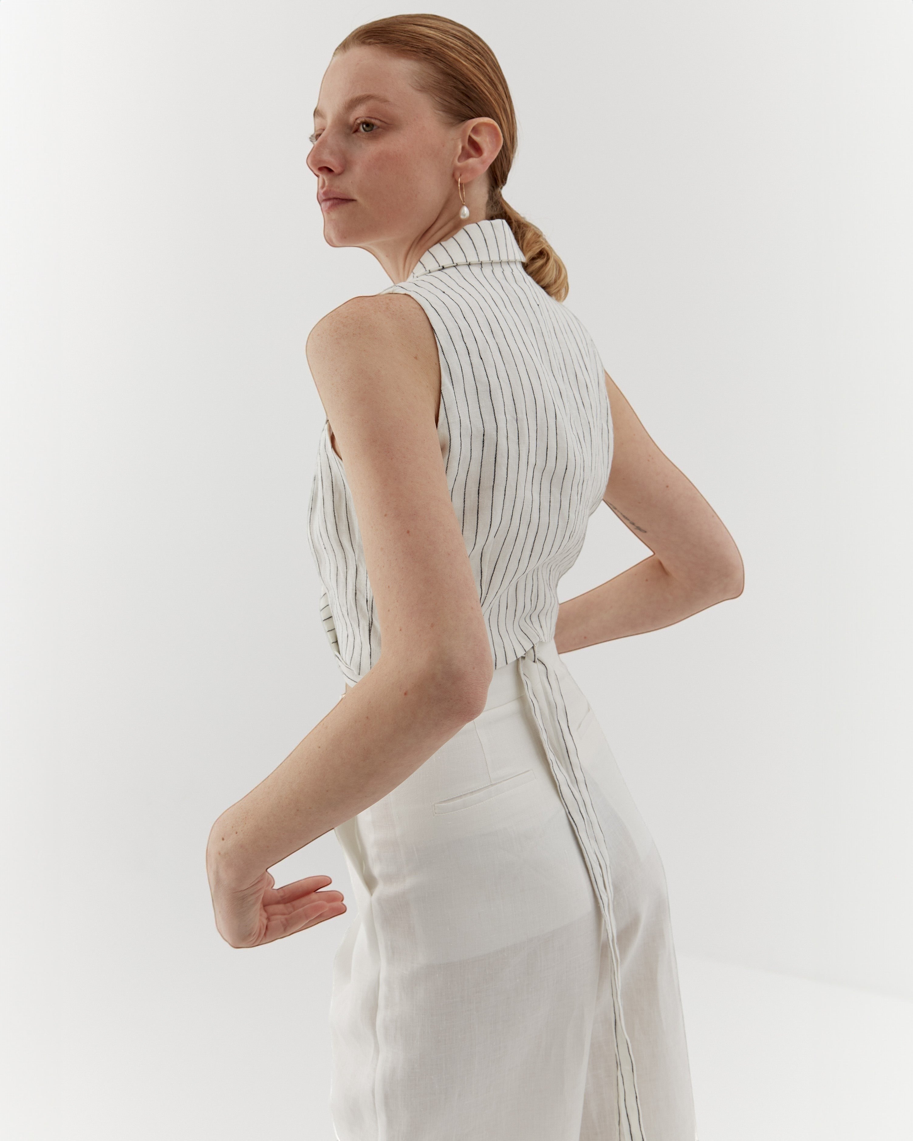 Ipanomi white linen vest with fine black pinstripes, featuring a wrap closure and adjustable tie.