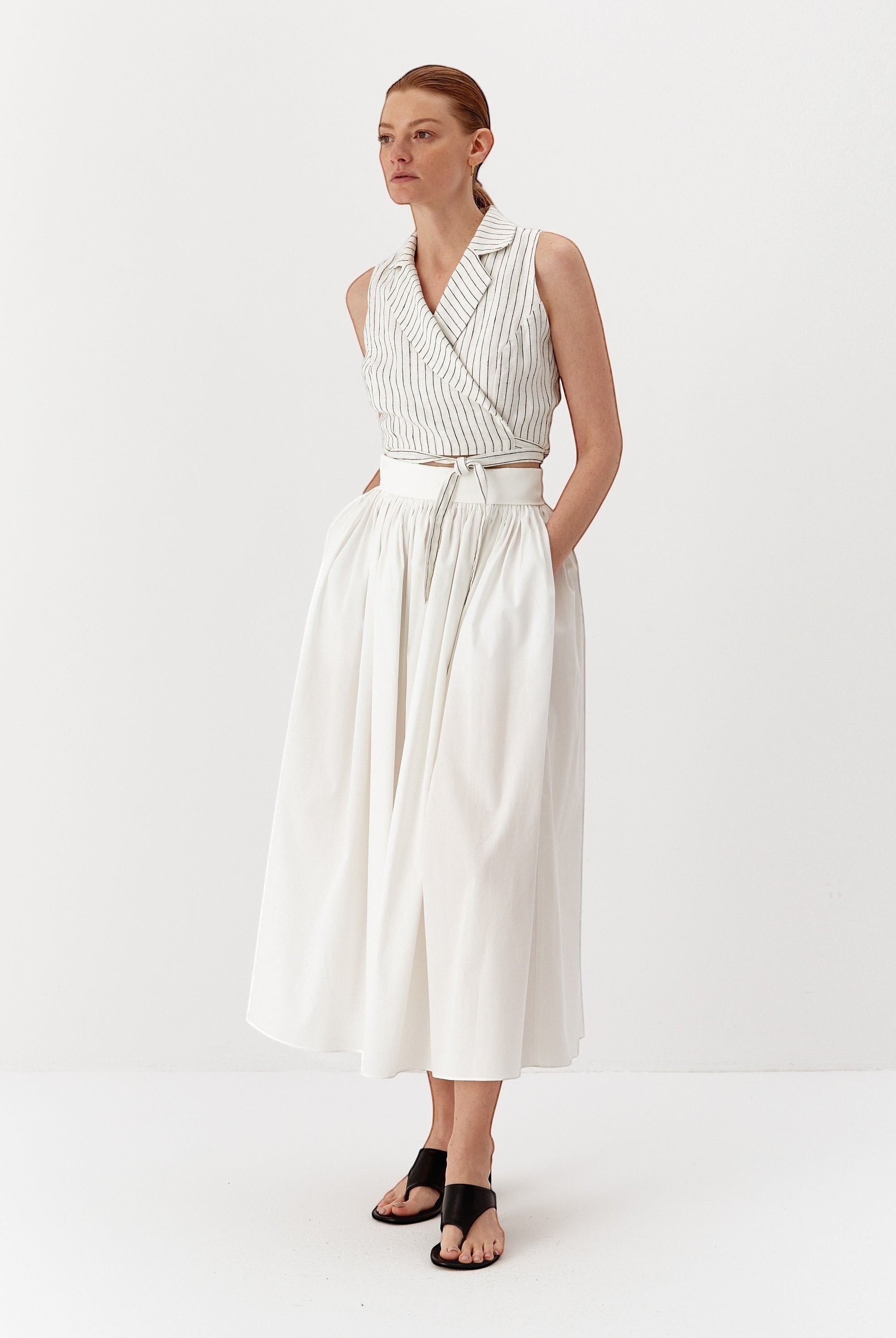 Ipanomi white linen wrap vest with fine black pinstripes, featuring a wide lapel and adjustable tie waist.