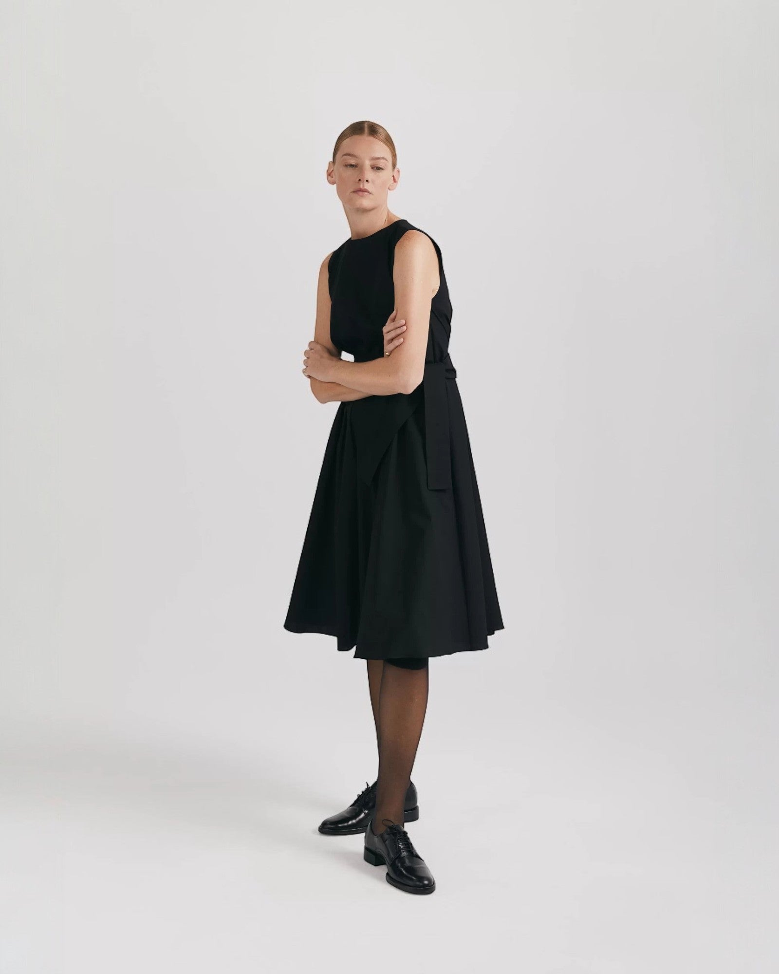 Ipanomi black organic cotton midi dress with flared skirt, pleats, and hidden pockets. Sleeveless, round neck, back zip.