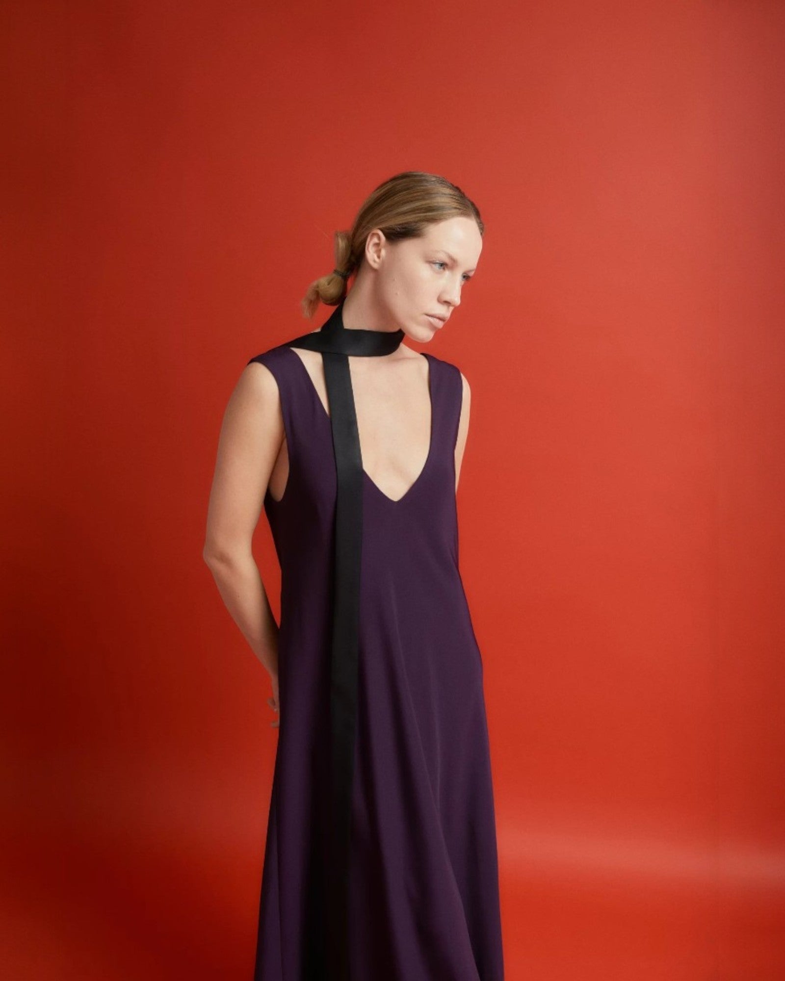 Ipanomi narrow black silk scarf worn as a necktie with a deep V-neck purple dress.