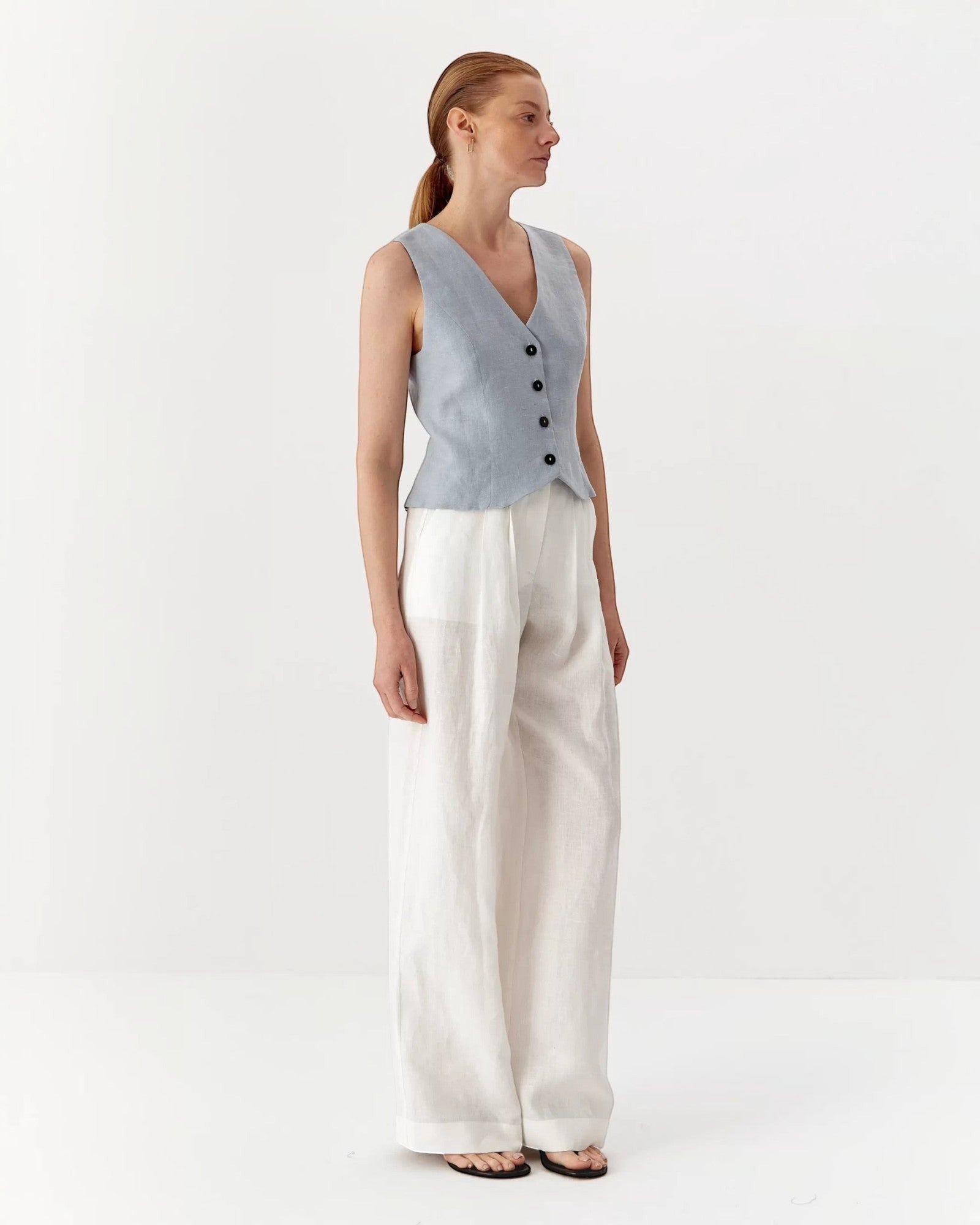 Ipanomi light blue pure linen short vest with V-neck and black buttons, worn by a model.