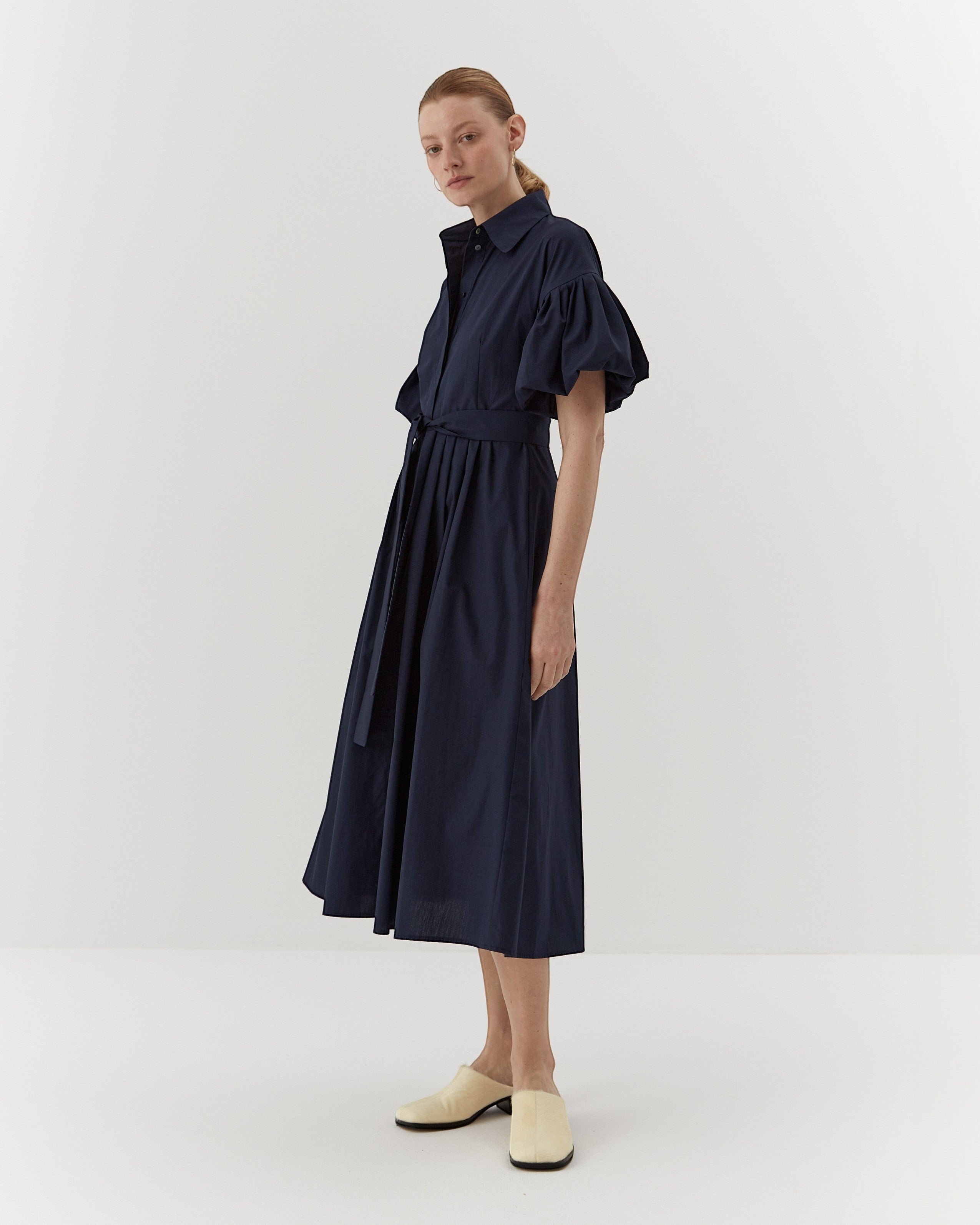 Ipanomi navy organic cotton midi dress with puffed sleeves, belted waist, and hidden pockets. Model is wearing size S.