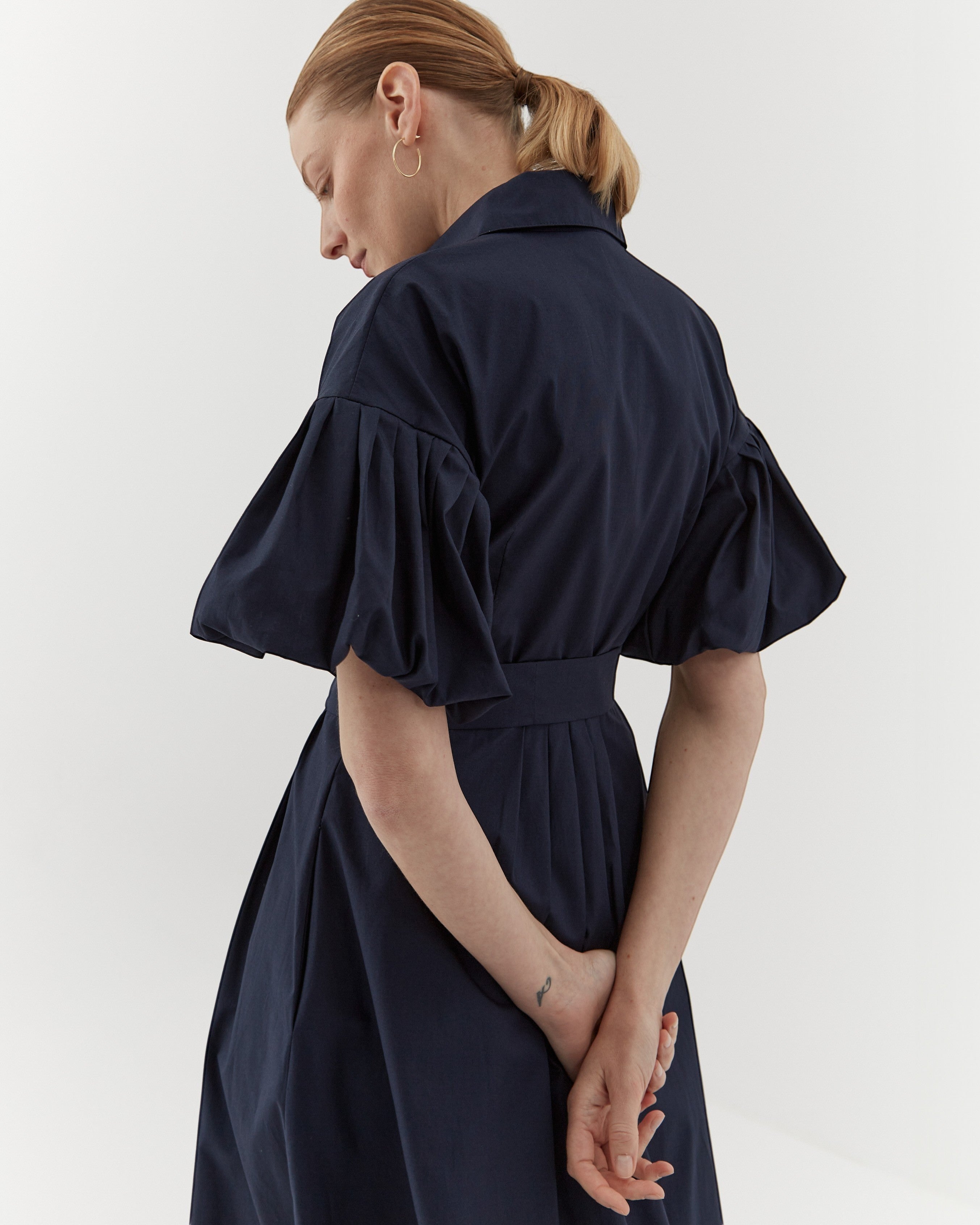 Ipanomi navy blue organic cotton midi dress with pleated sleeves, defined waist, and hidden pockets. Model wears size S.