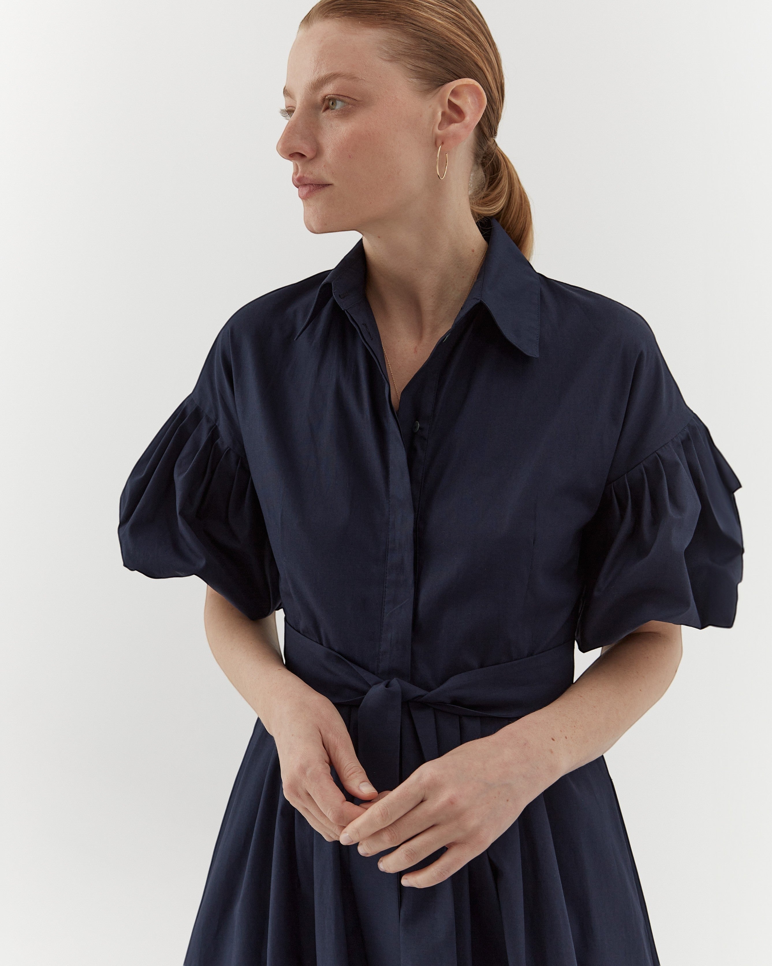 Ipanomi navy organic cotton midi dress with puffed sleeves, belted waist, and hidden pockets. Model wears size S.