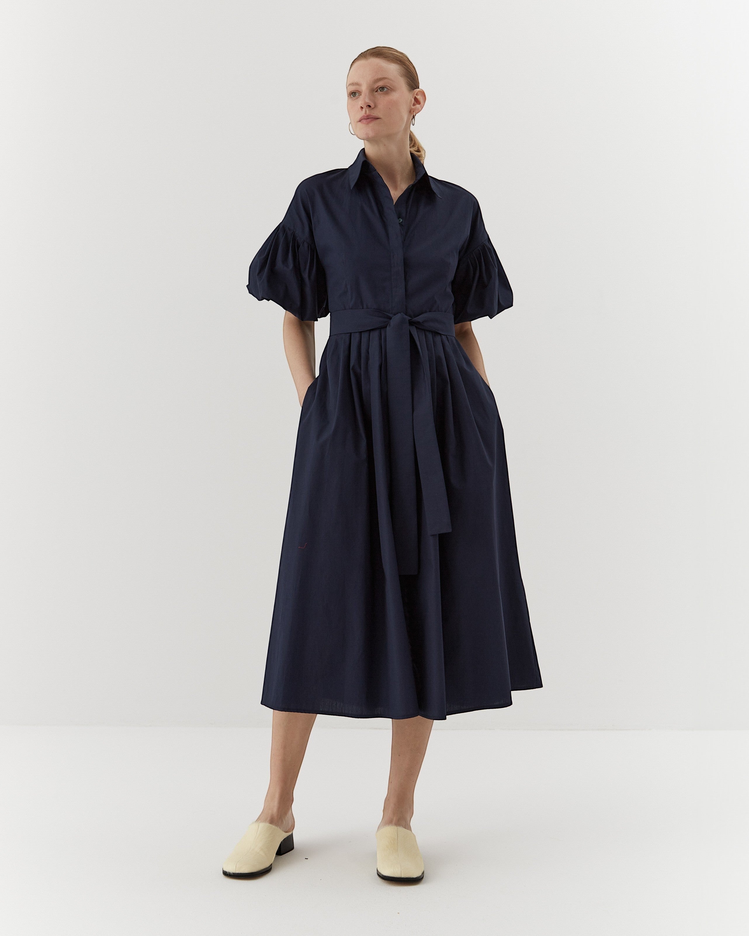 Ipanomi navy blue organic cotton midi dress with puffed sleeves, belted waist, and hidden pockets. Model wears size S.