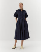 Ipanomi navy blue organic cotton midi dress with puffed sleeves, belted waist, and hidden pockets. Model wears size S.