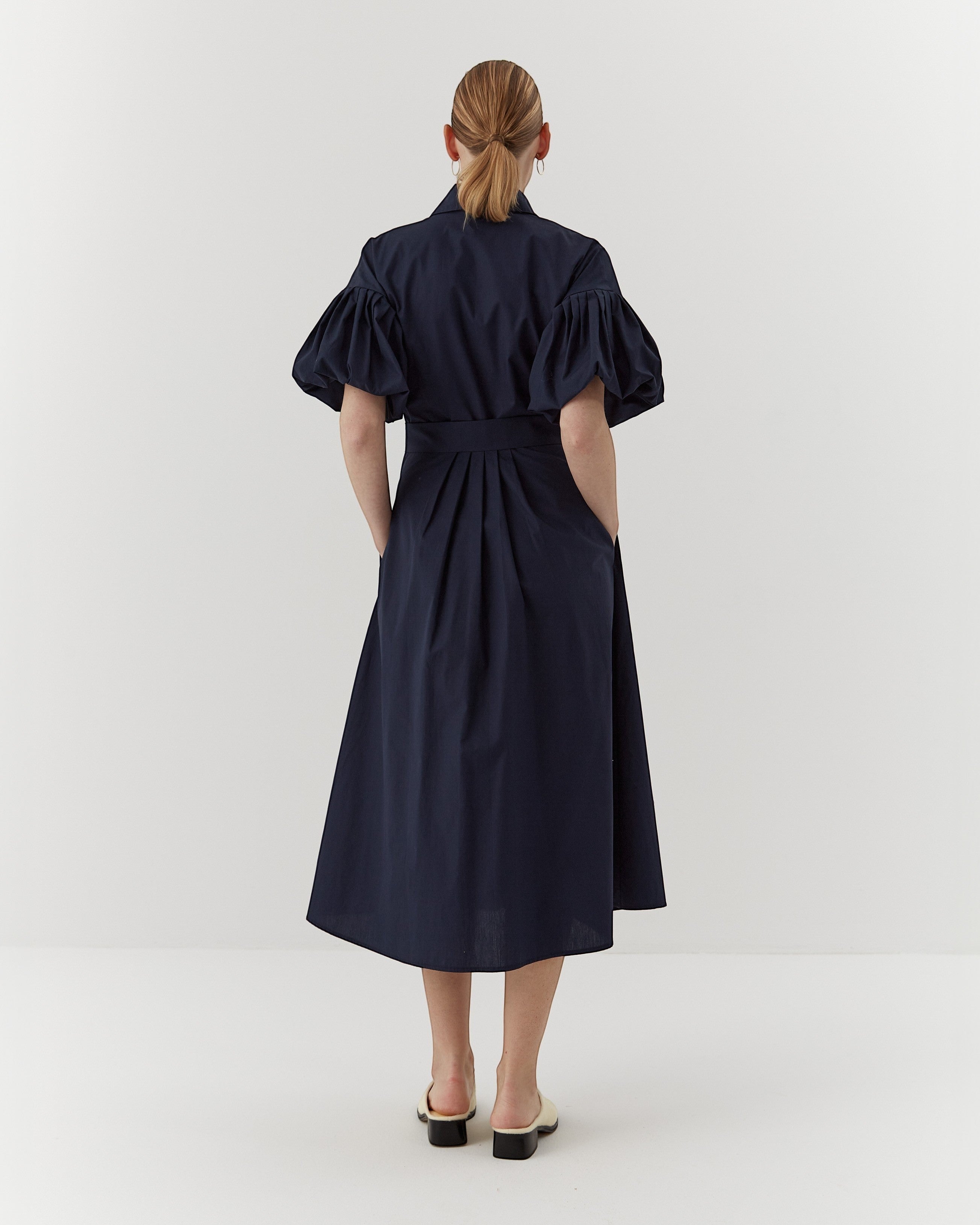 Ipanomi navy organic cotton midi dress with puffed sleeves, belted waist, and pleats. Model wears size S.