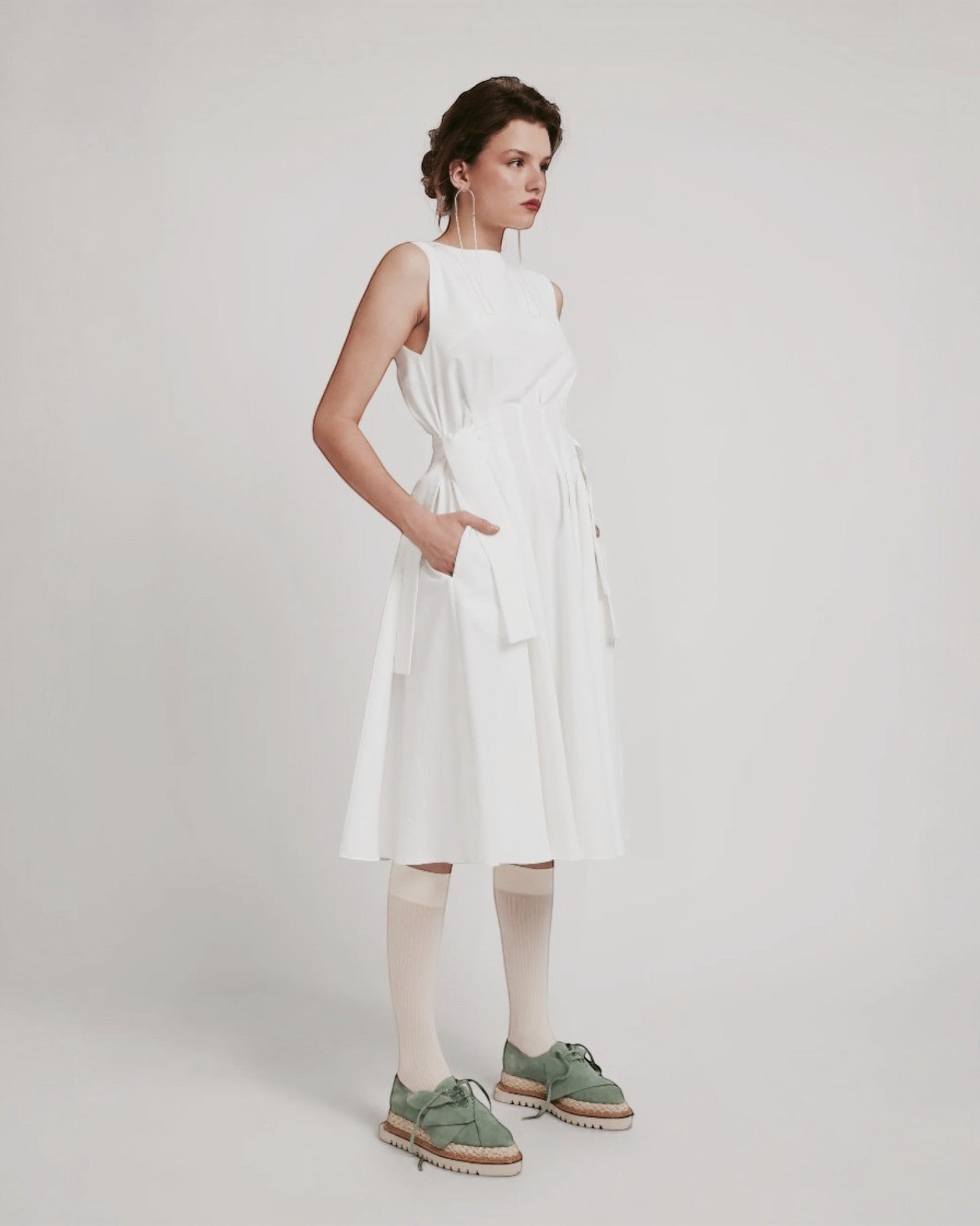 Ipanomi white cotton midi dress with adjustable waist ties, sleeveless design, and hidden side pockets. Perfect for elegant occasions.