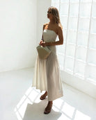 Ipanomi strapless white cotton poplin corset and maxi skirt set with a straw and leather handbag.