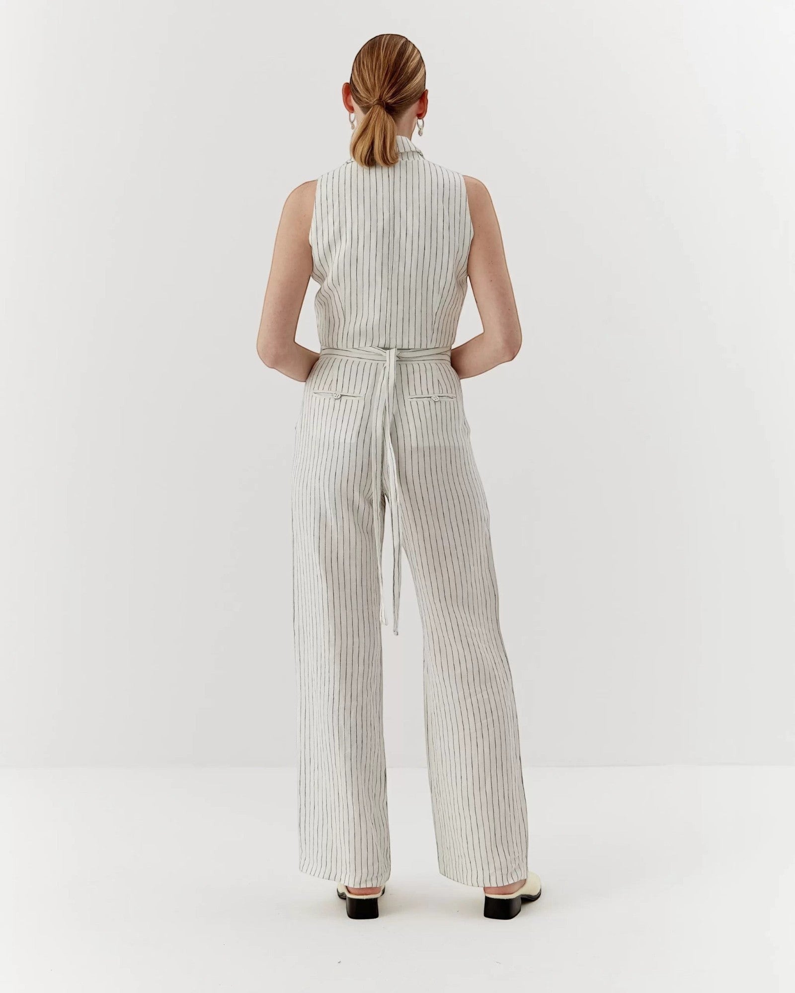 Ipanomi white linen trousers with black pinstripes, high waist, straight leg, and tie belt. Model is wearing size S.