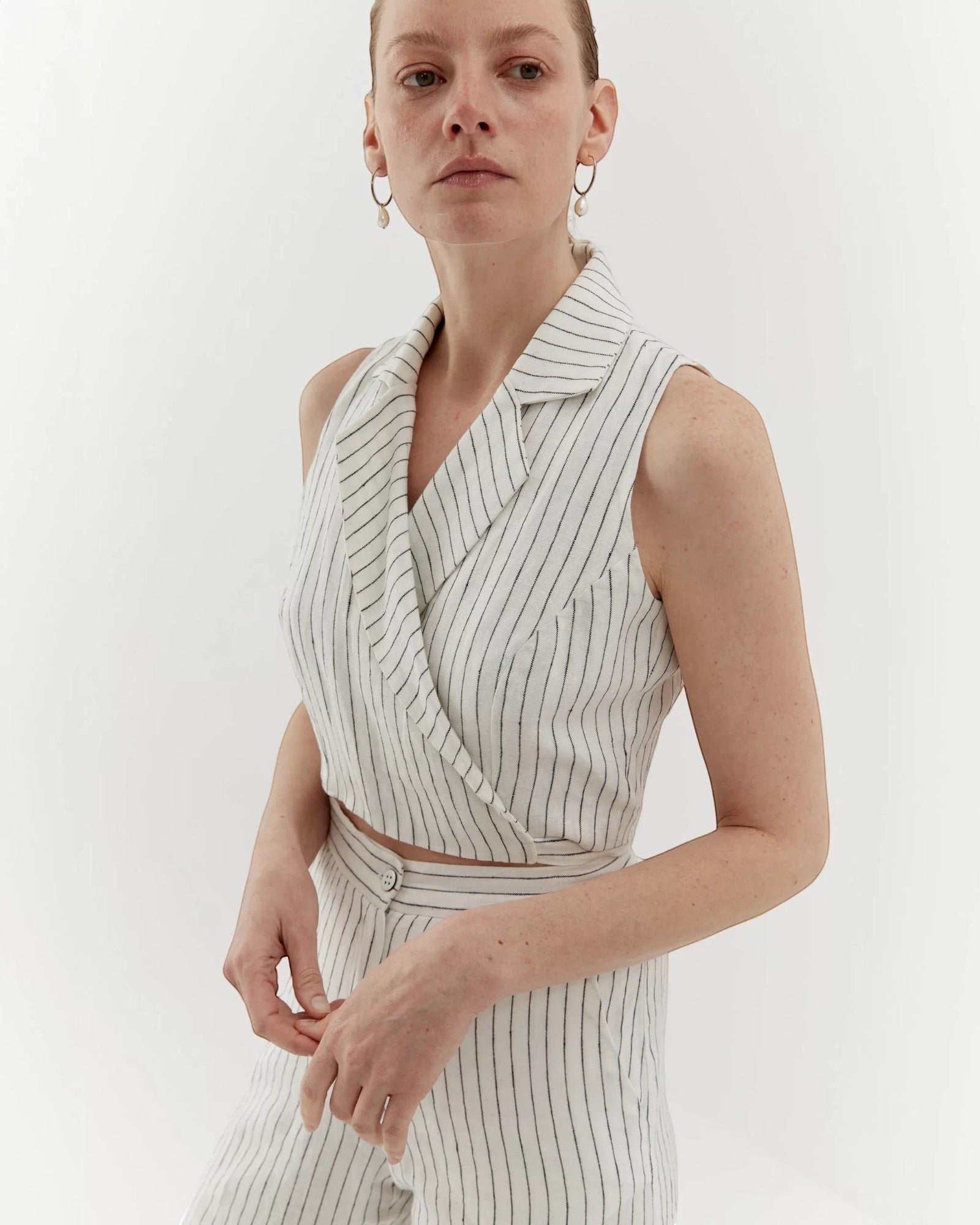 Ipanomi white linen trousers with black pinstripes, high-waisted, straight leg, and side pockets. Model wears size S.