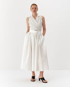 Ipanomi white linen wrap vest with fine black pinstripes and a tie waist, paired with a white midi skirt.