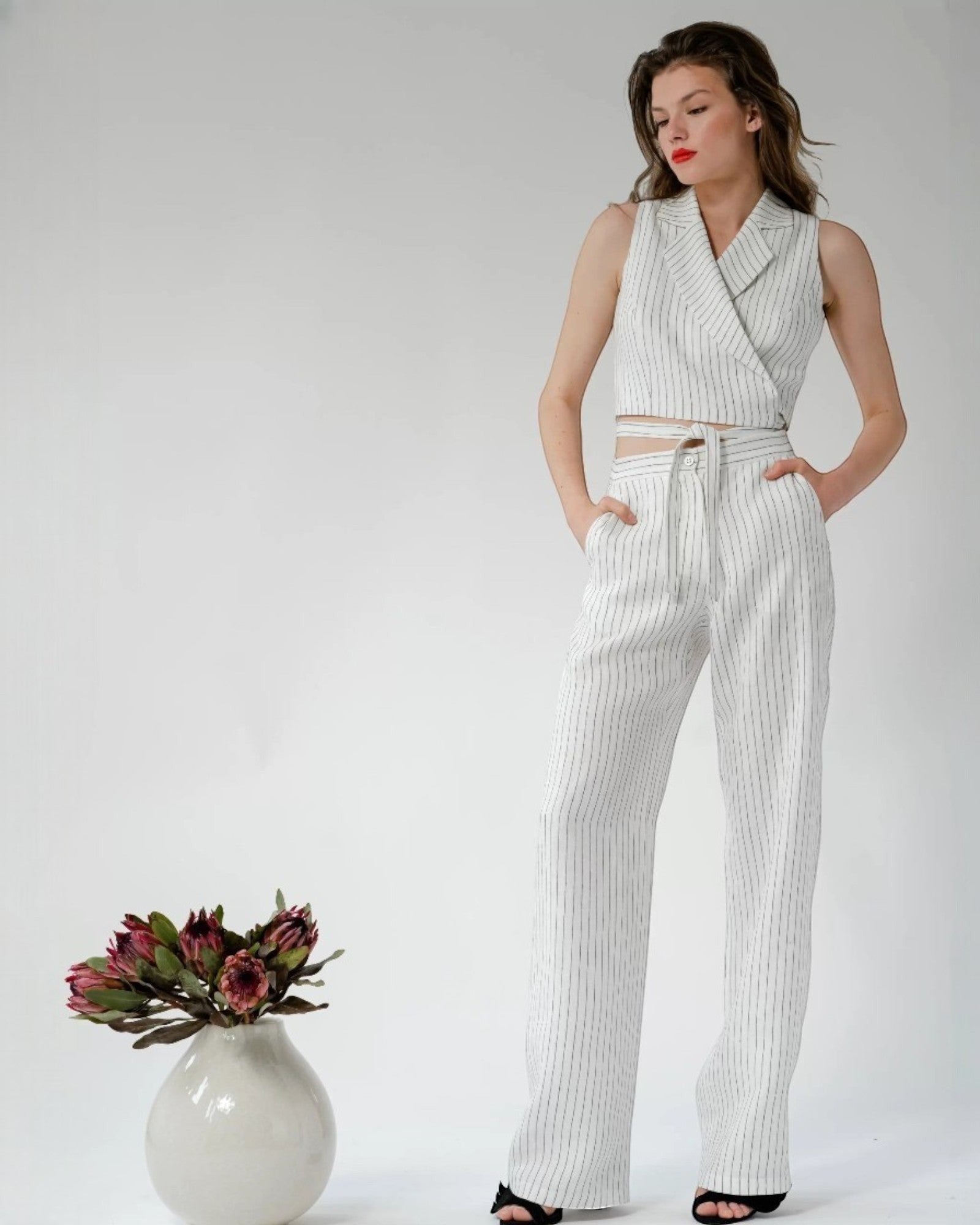 Ipanomi white pinstripe sleeveless cropped blazer top with a tie waist and lapel collar.