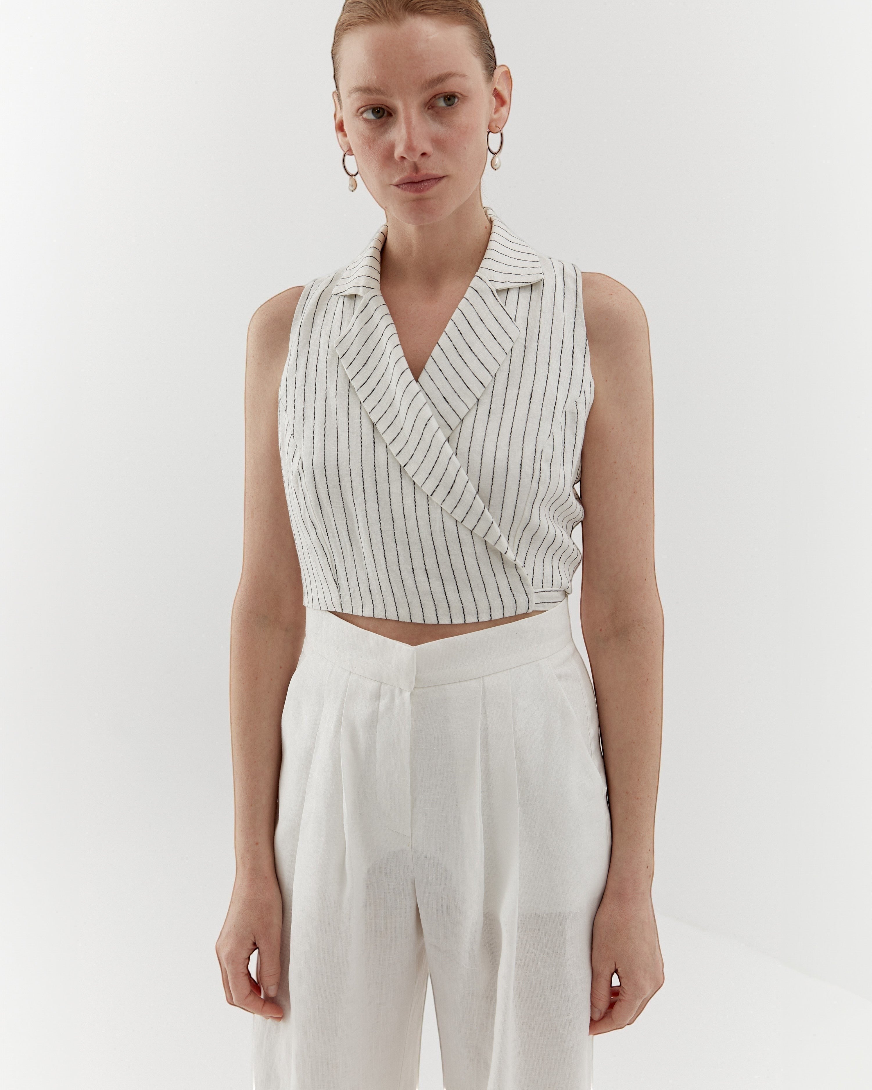 Ipanomi white linen vest with fine black pinstripes, featuring a wrap front and lapel collar.