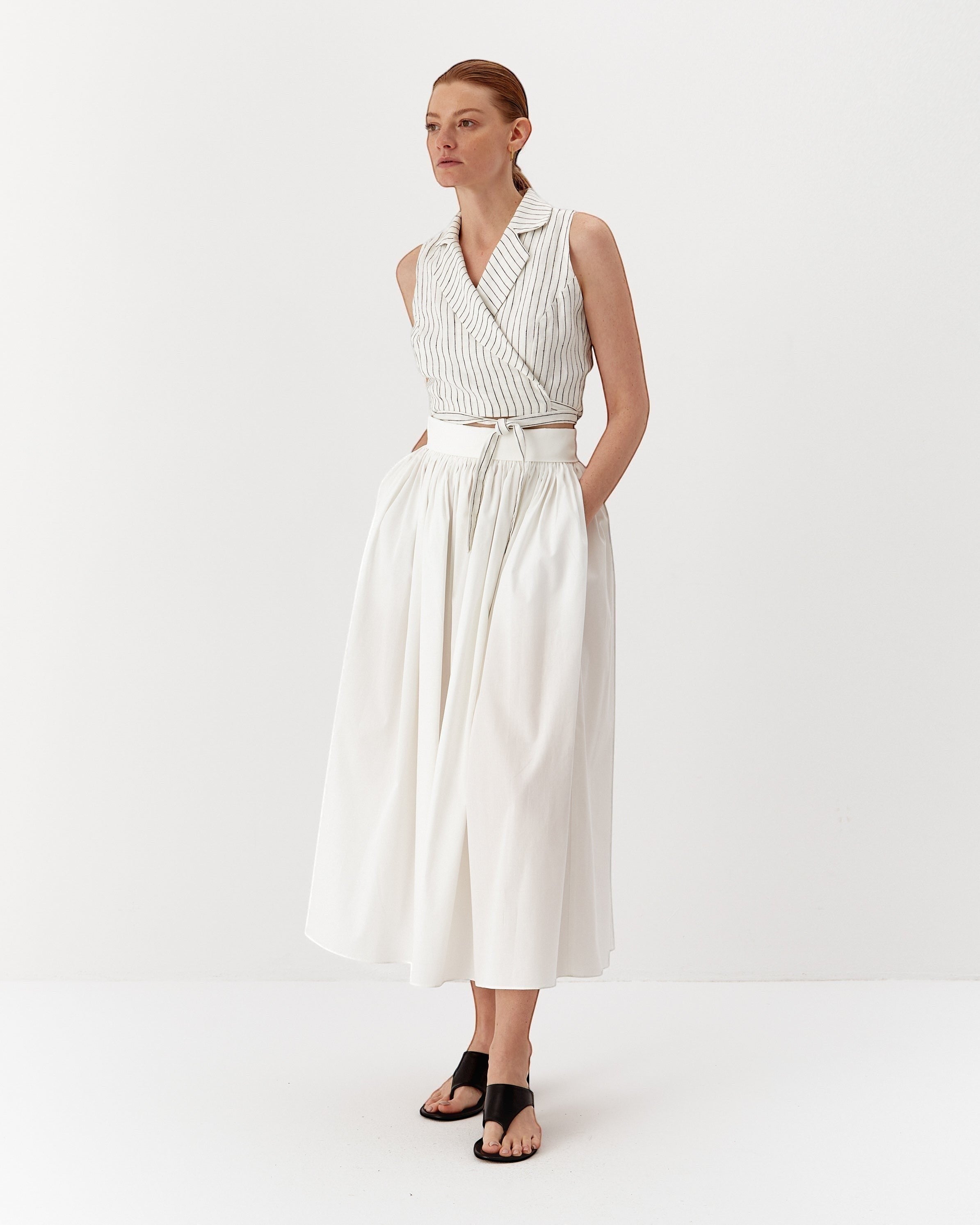 Ipanomi white linen wrap vest with fine black pinstripes, featuring a wide lapel and adjustable tie waist.